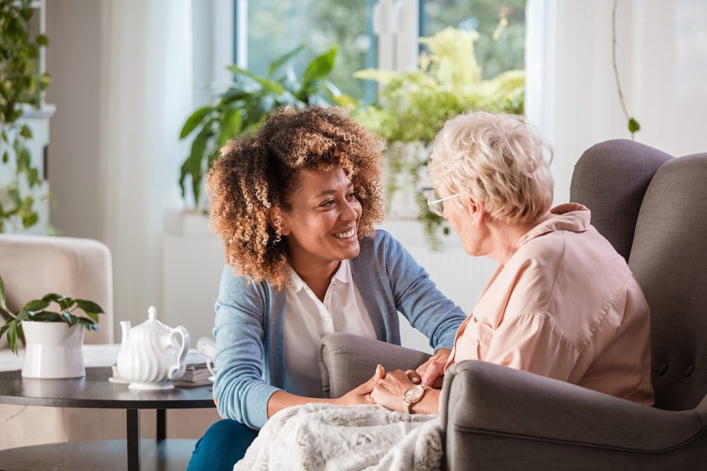 A social worker sitting beside an older woman in her living room, holding her hand as they talk
