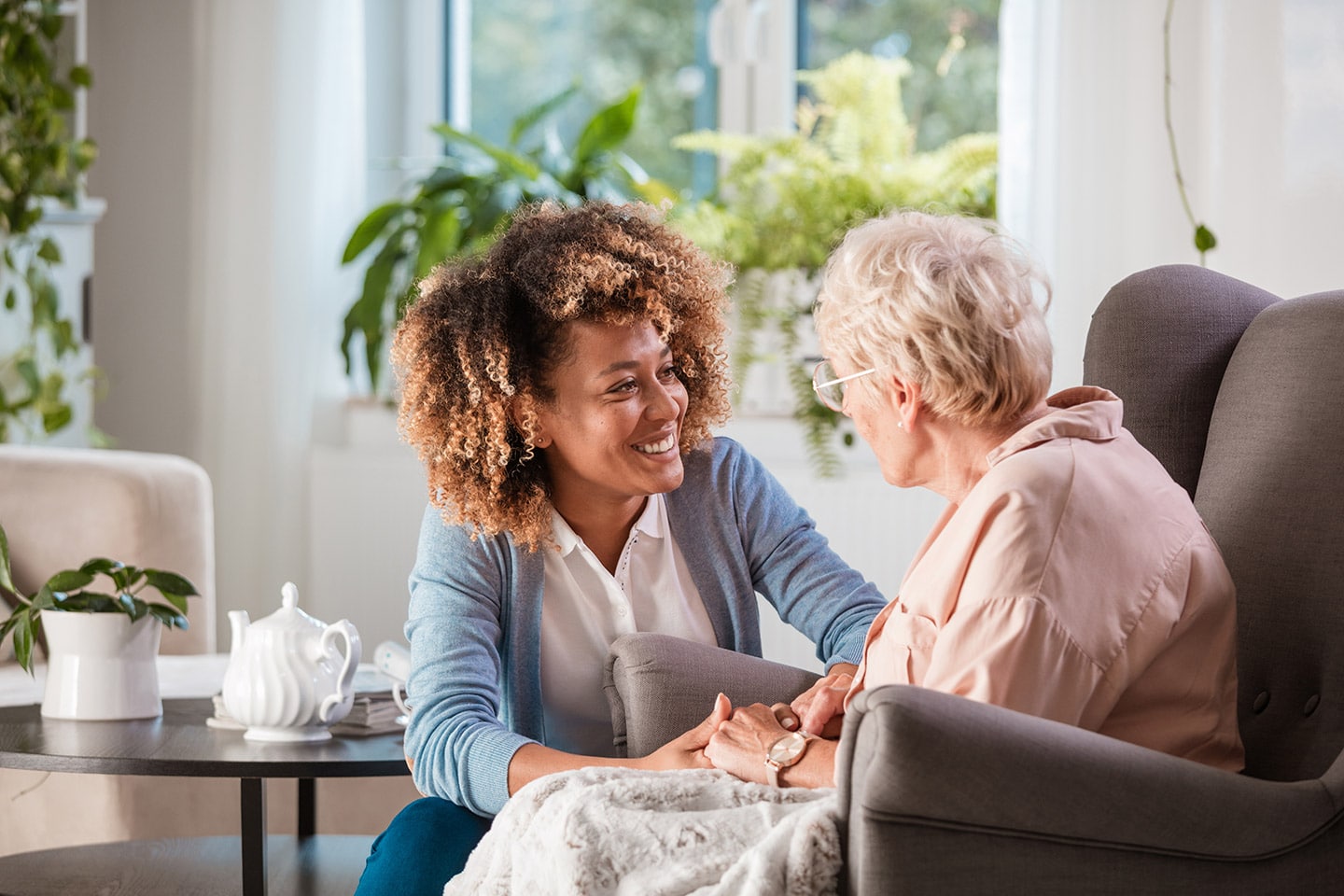 A social worker sitting beside an older woman in her living room, holding her hand as they talk