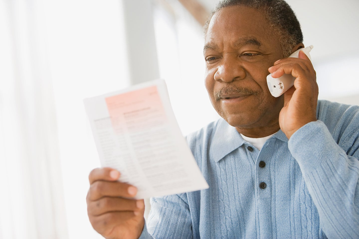 An older man on the telephone, reading a printed information sheet