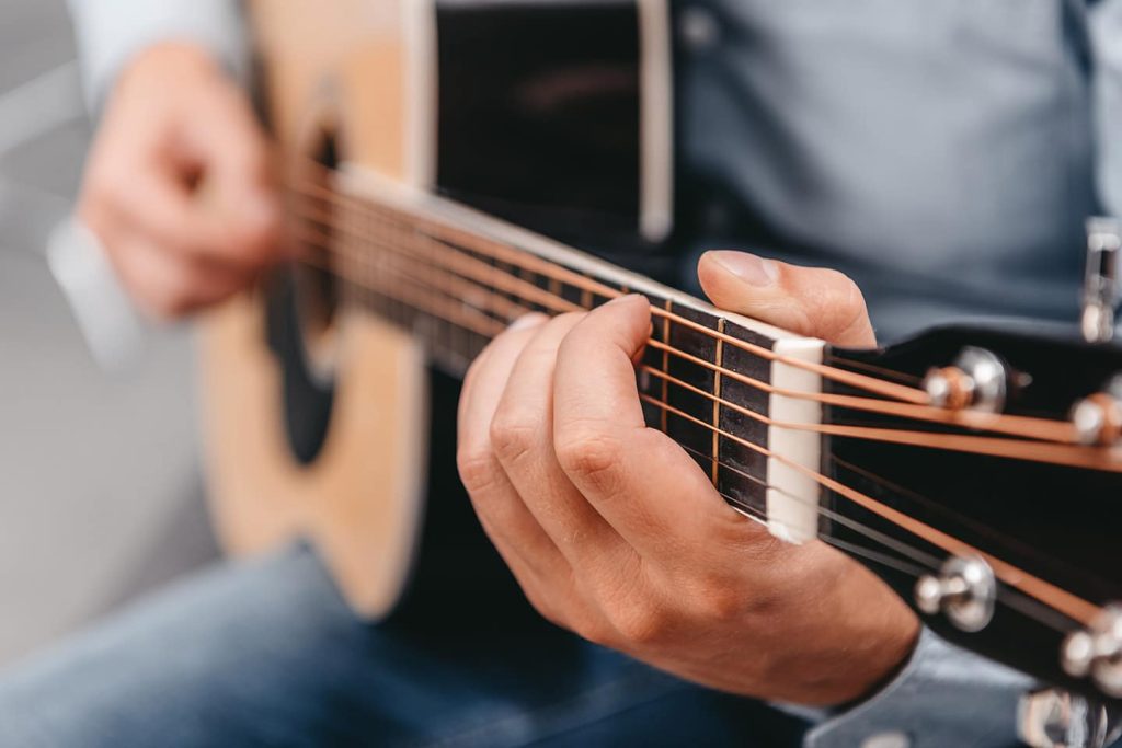 A seated musician fingering a chord on an acoustic guitar, hands close in the frame