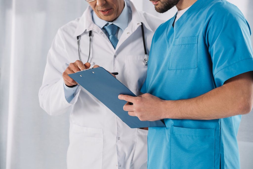 A physician in a white coat and a nurse in scrubs standing together, reading notes on a clipboard