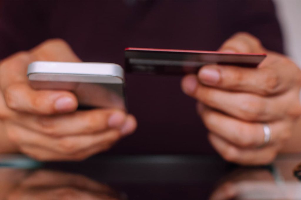 A person holding a phone in one hand and a credit card in the other