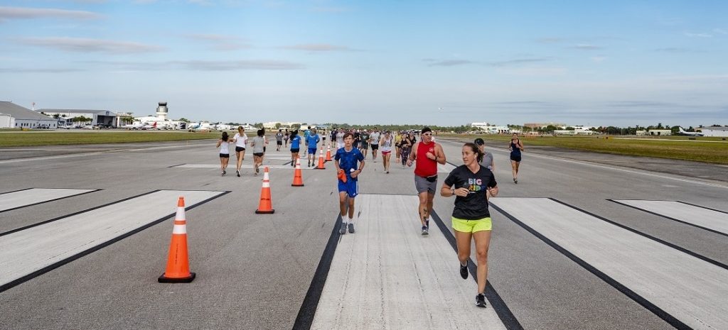 Runners spread across an airport runway during the Uptown 5K on the Runway, with parked aircraft in the distance