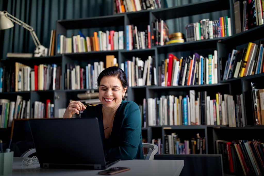 A woman working at a laptop at a desk in a book-lined office