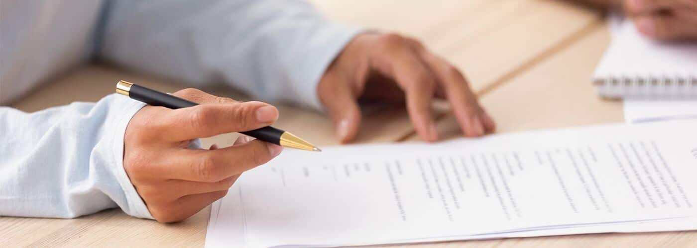 Hands holding a pen over a printed agreement on a desk