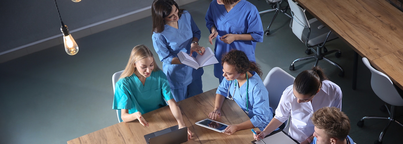 Clinicians in scrubs gathered around a table with notes and a tablet