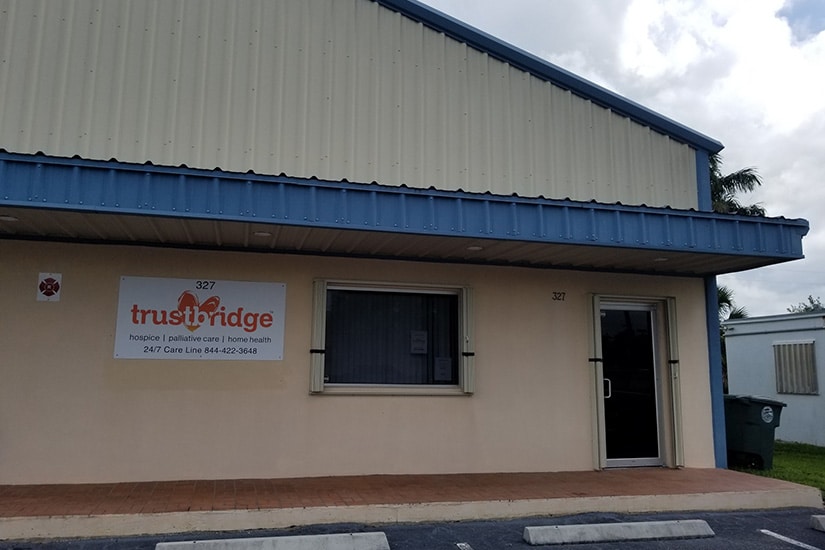 The Belle Glade office, a beige single-storey building with a blue roof and a Trustbridge sign beside the door