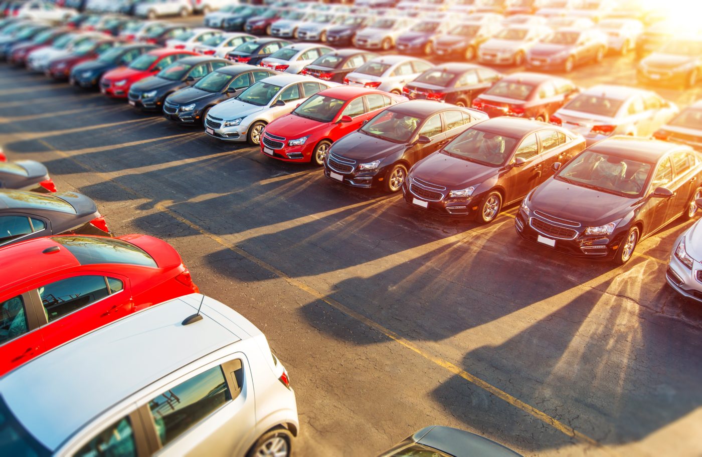 Rows of cars parked in a dealership lot, lit low by the sun