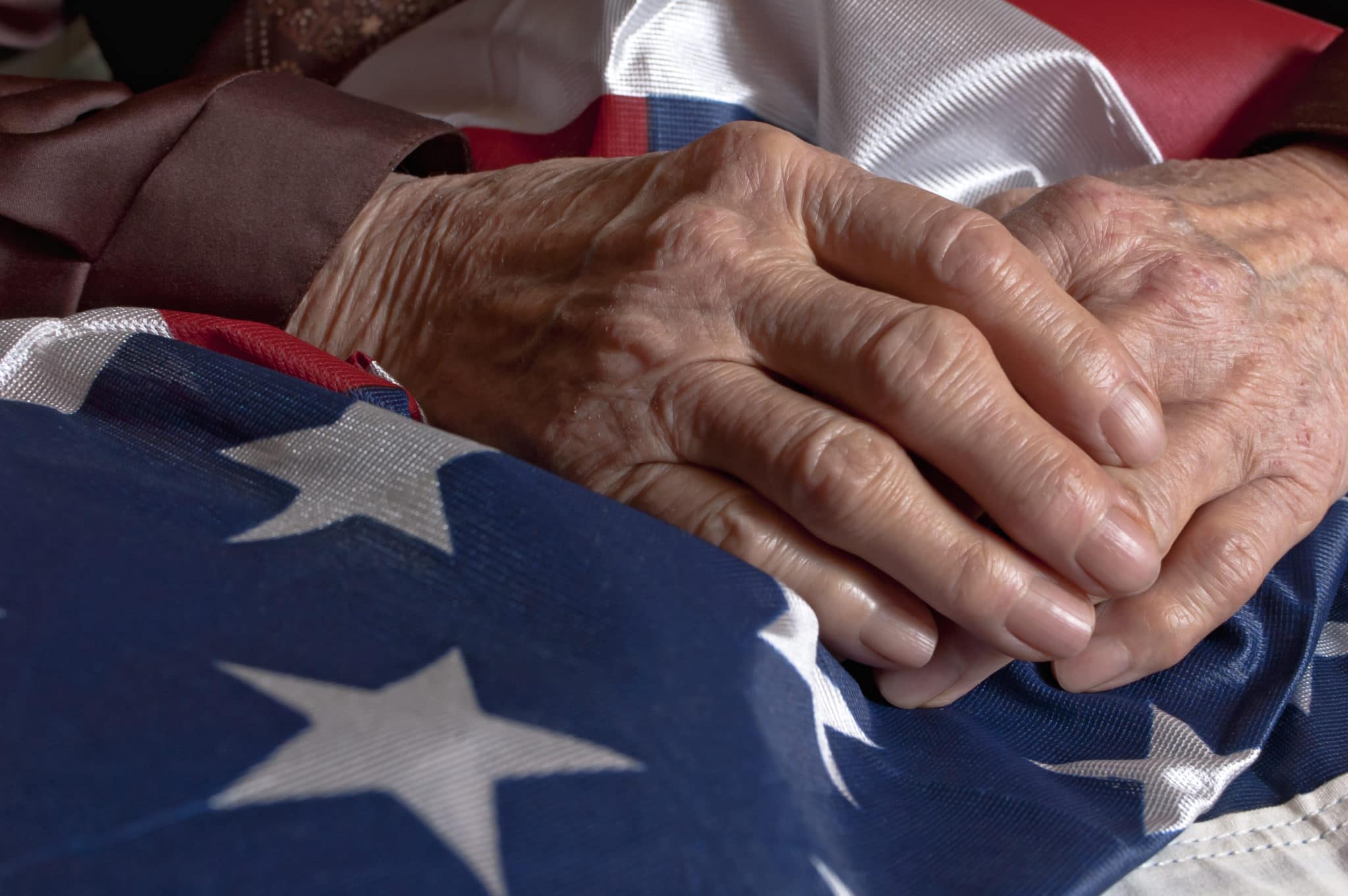 The folded hands of an older person resting on a folded United States flag