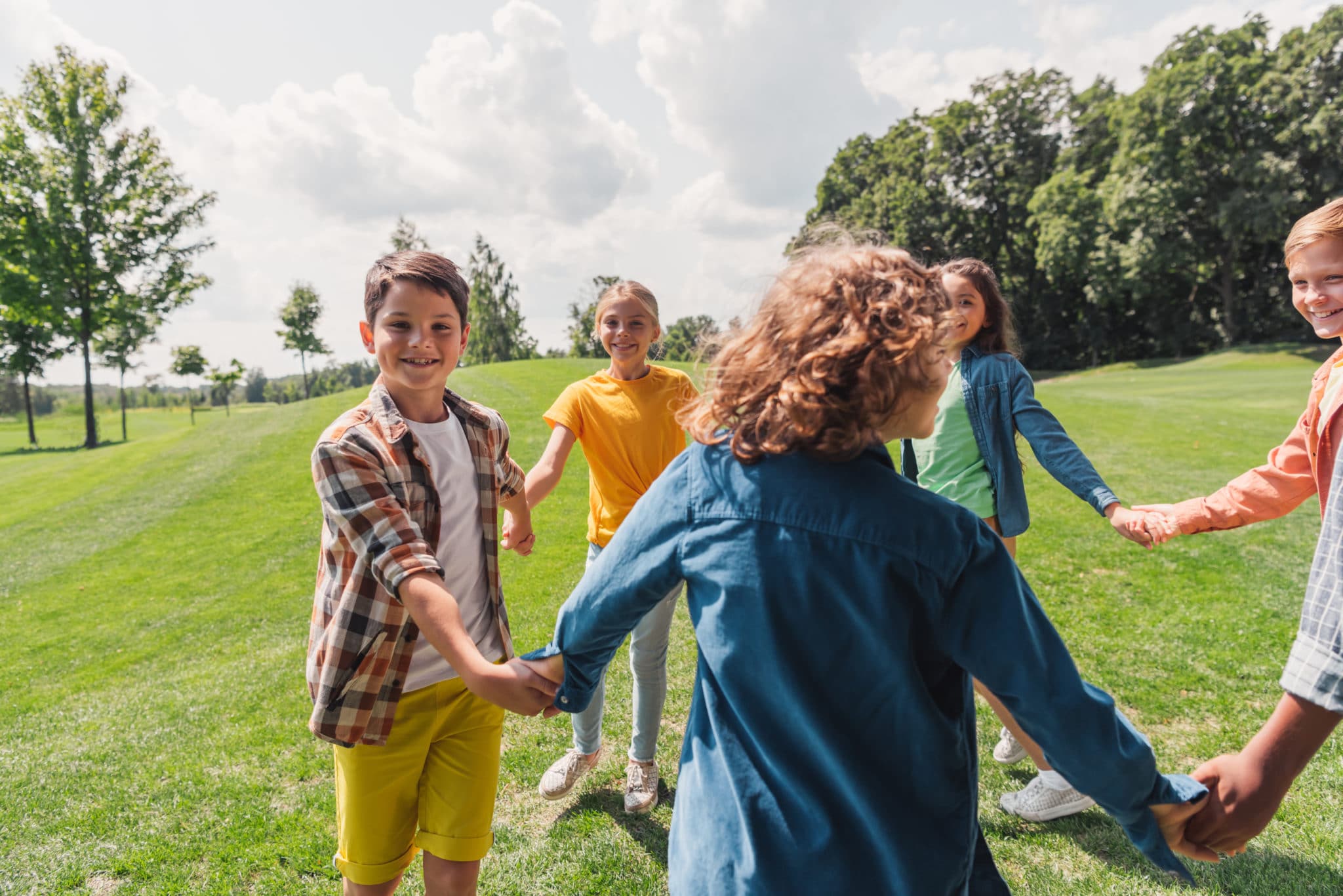 Children holding hands in a circle on a grassy field, laughing together