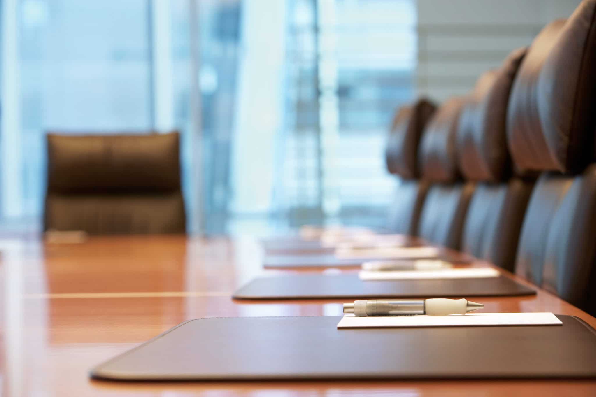 An empty boardroom table with leather chairs, notepads and pens set out