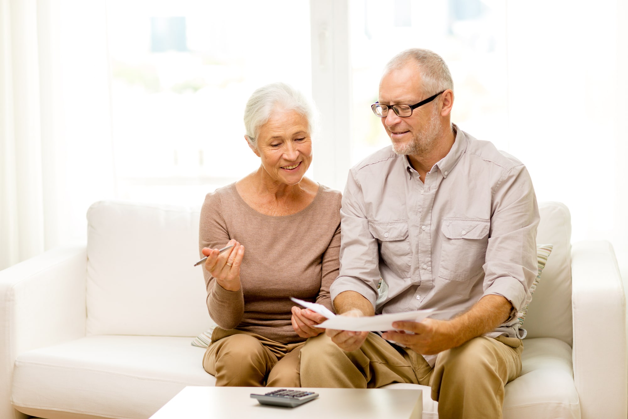 An older couple sitting together on a sofa at home, reading through paperwork.