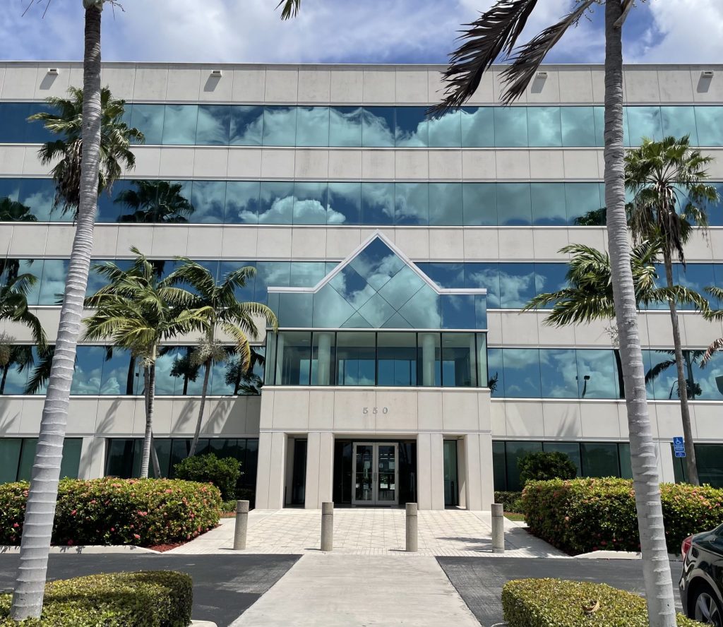 The glass-fronted office building numbered 550 on West Cypress Creek Road, with palm trees at the entrance