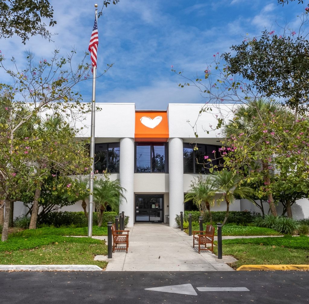 The two-storey white entrance to the Charles W. Gerstenberg Hospice Center, an orange panel with a white heart above the doors and a bench on each side of the walkway