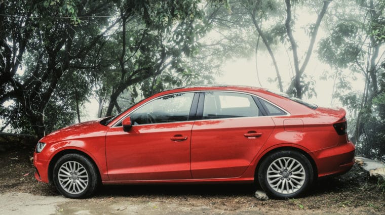 A red sedan parked on a wooded roadside