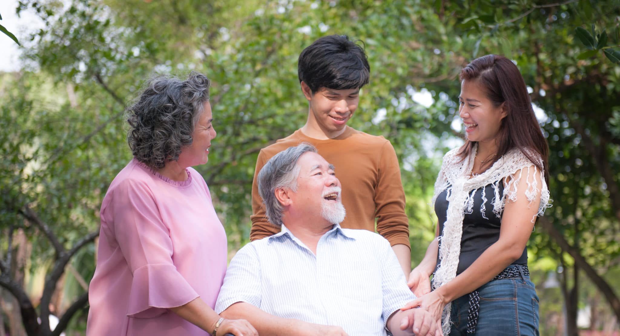 Three generations of a family gathered around a smiling older man seated outdoors, all laughing together