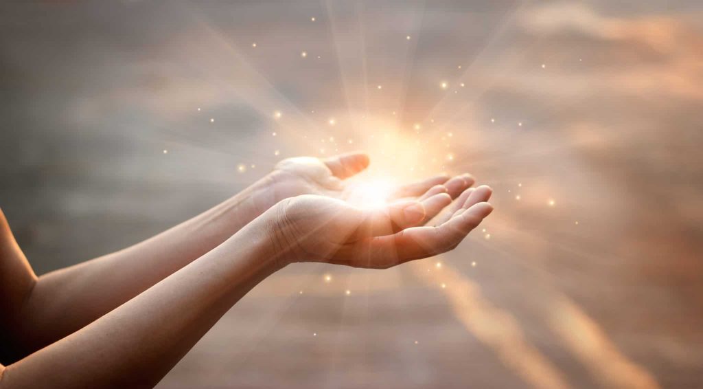 A pair of open hands cupped around a point of warm light at dusk
