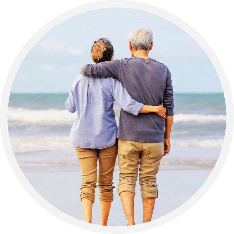 Two people walking arm in arm along the shoreline, seen from behind