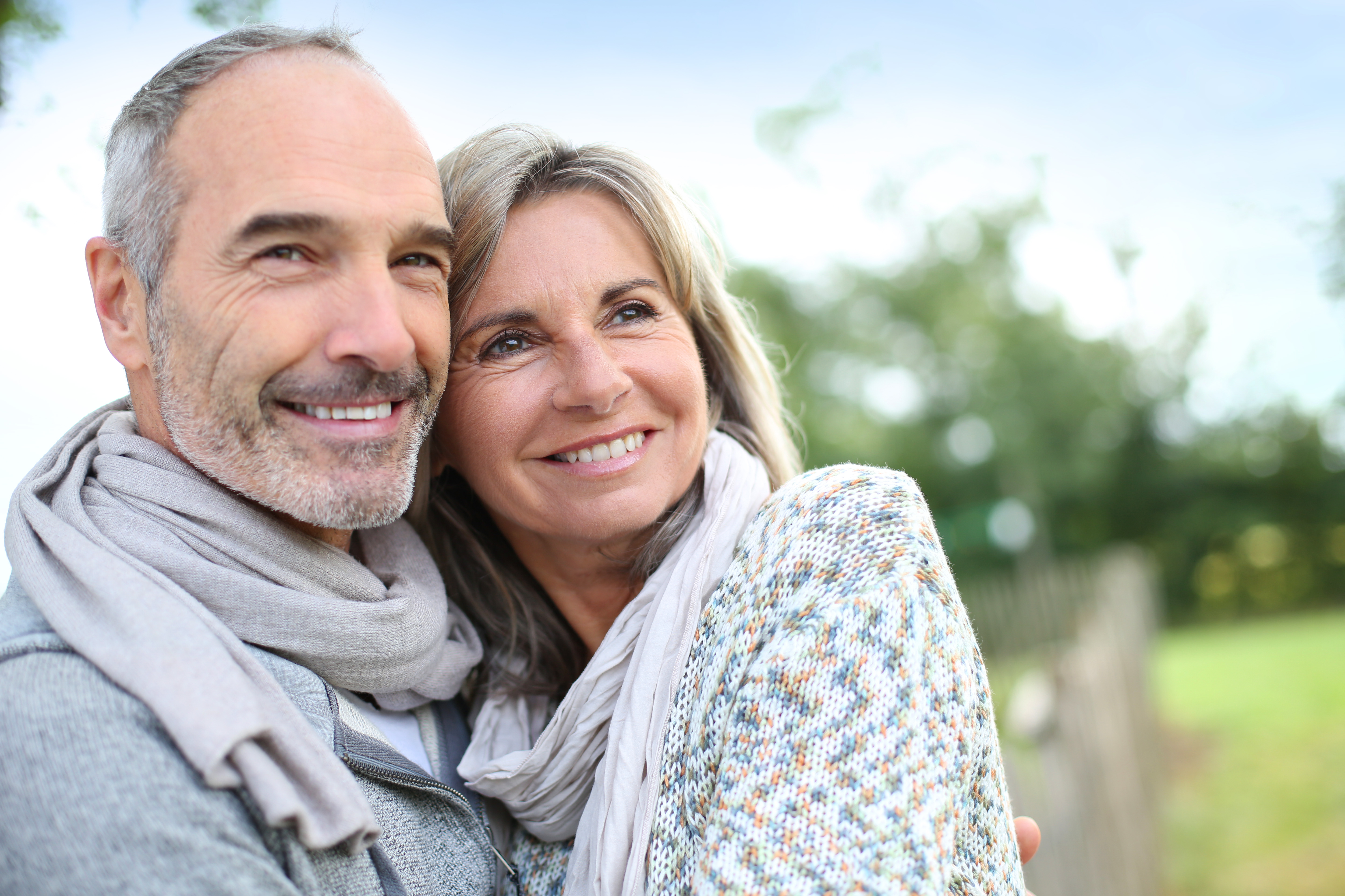 An older couple standing close together outdoors, smiling and looking into the distance