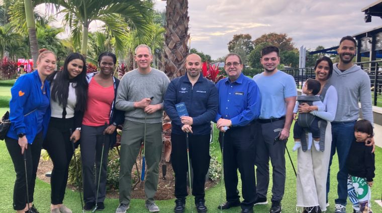 Eleven fellows, staff and family members with putters on a mini-golf course at a wellness outing