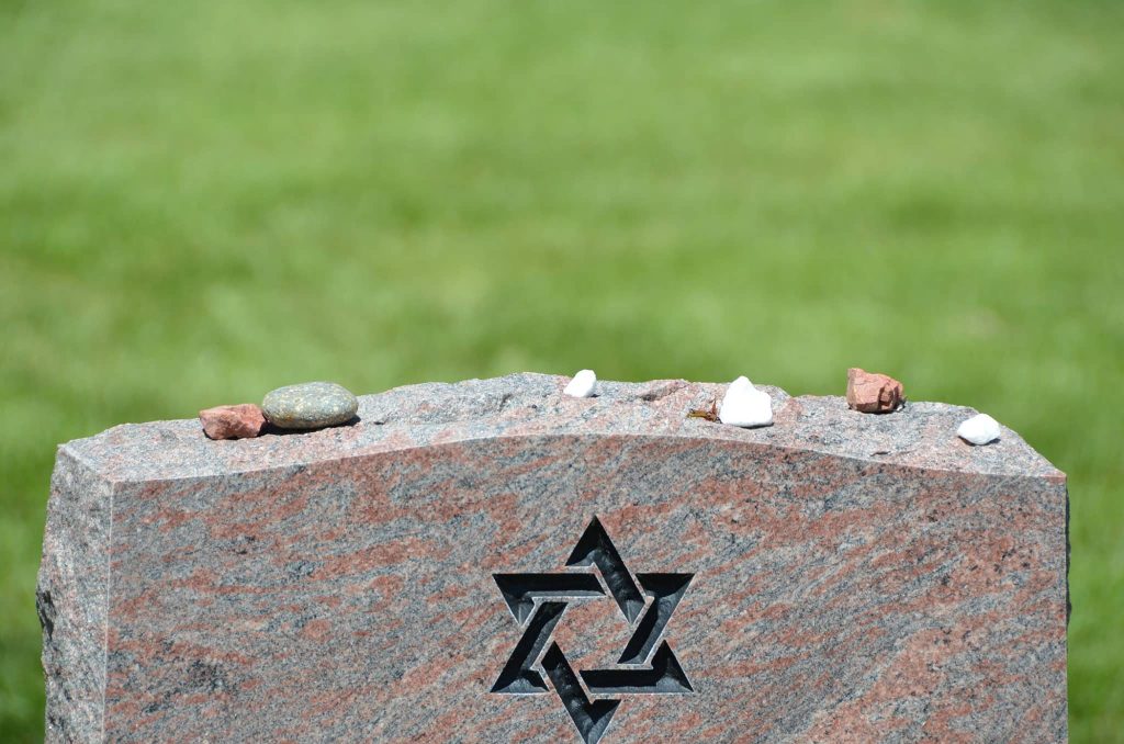 Small memorial stones resting along the top of a granite headstone carved with a Star of David