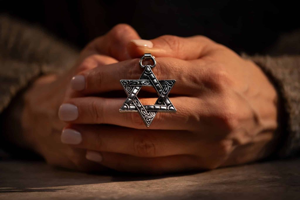 A pair of hands folded together around a silver Star of David pendant
