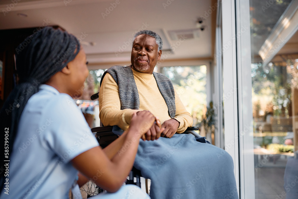 A nurse holding hands with a patient in a wheelchair beside a sunlit window